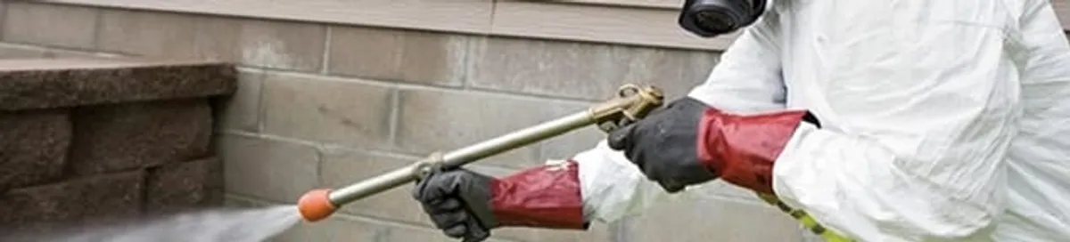 Pest control technician applying exterior insect treatment along a home foundation in Wilmington, NC