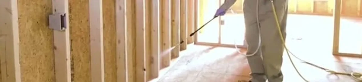 Termite treatment technician applying spray along framing and unfinished walls in Wilmington, NC